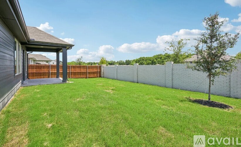 A backyard with a fence, a small tree, and a covered patio area.
