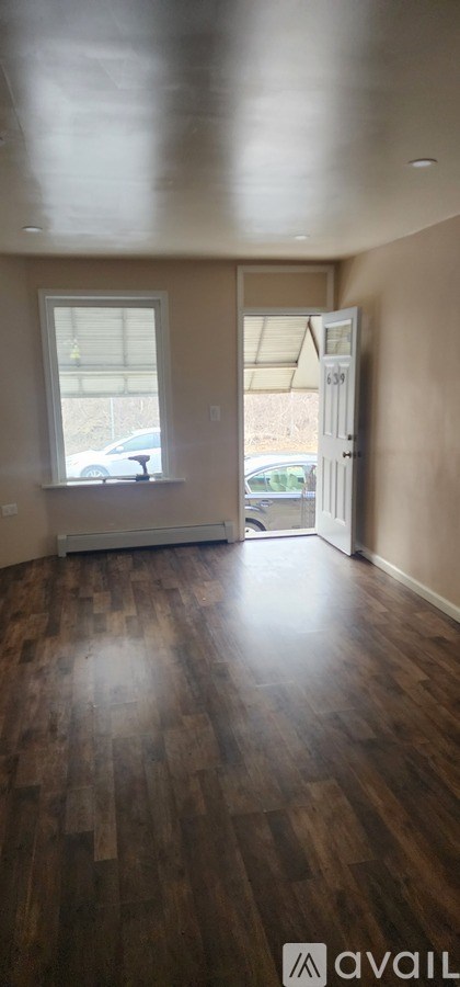 A room with wooden floors and a window overlooking a parking lot.
