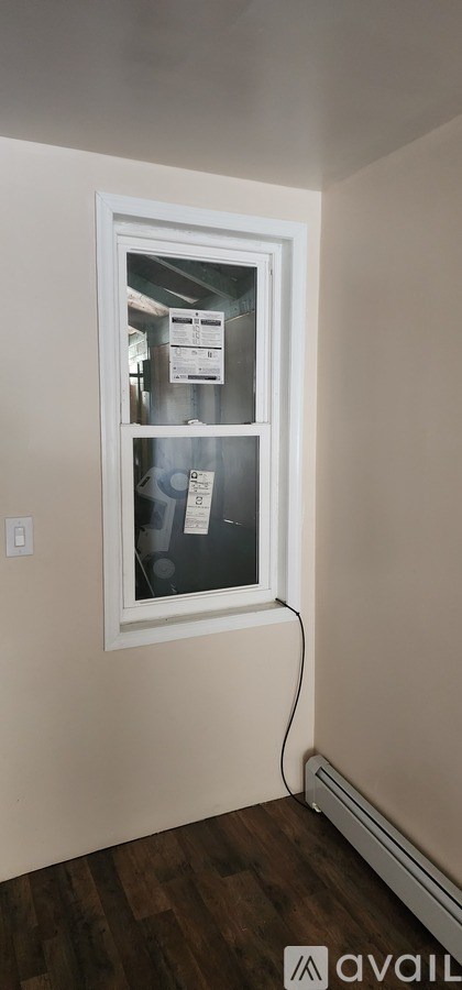 A window with a white frame is installed in a room with wooden flooring.