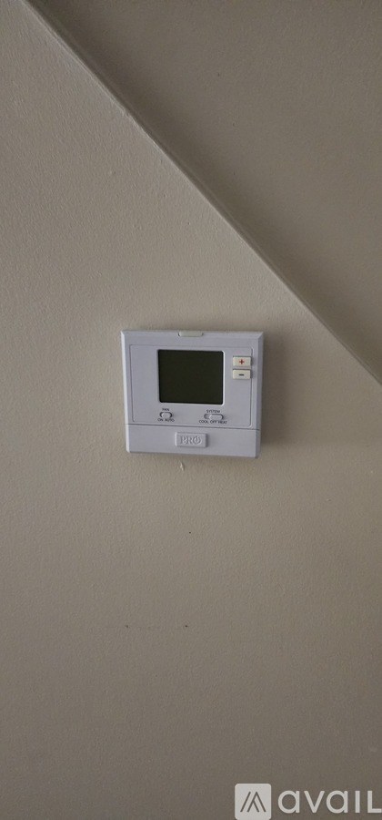 A white thermostat is mounted on a beige wall.