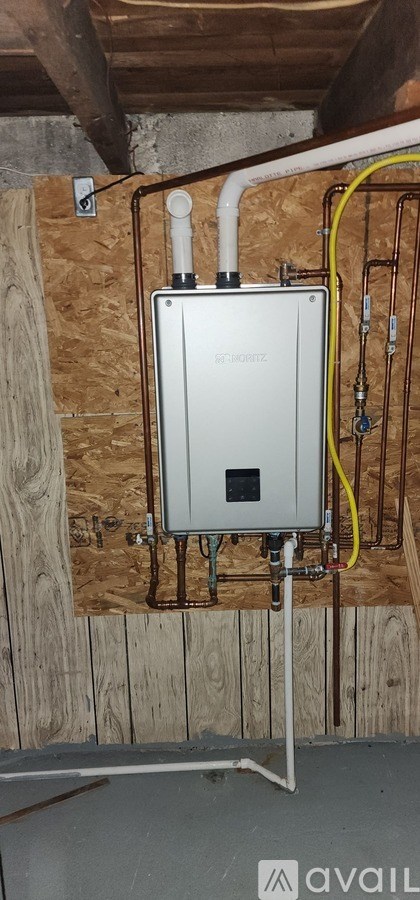 A tankless water heater is installed in a room with wooden walls.