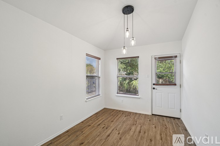 A room with wooden floors and white walls, two windows with blinds, and a door.