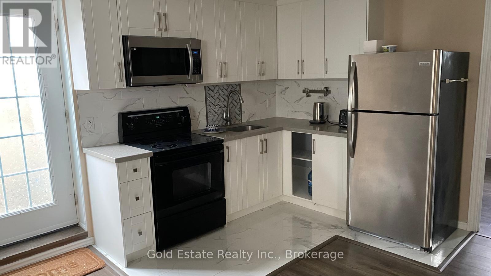A kitchen with a refrigerator, microwave, oven, and sink.