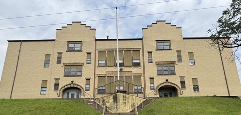 A large, beige building with a symmetrical facade and a set of stairs leading up to the entrance.