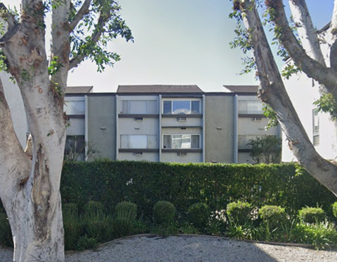 A building with a grey facade is surrounded by trees and bushes.