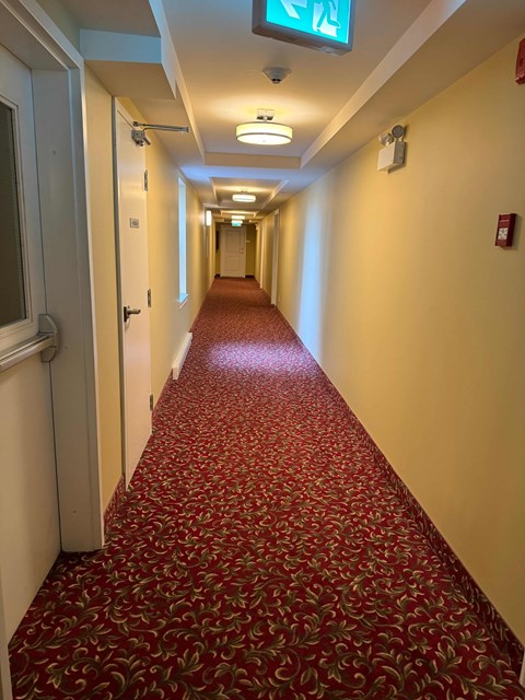 A long hallway with a red carpet and a green exit sign.