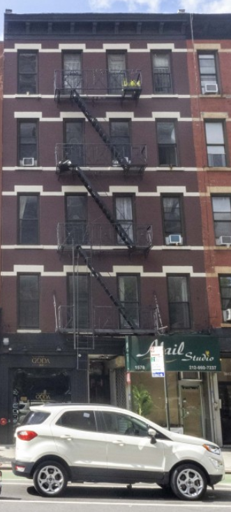 A white car is parked on the street in front of a red brick building.