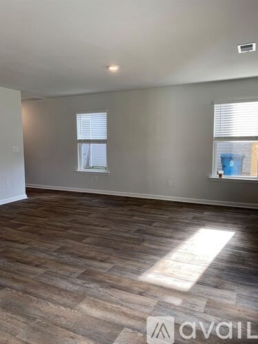 A room with wooden flooring and two windows.
