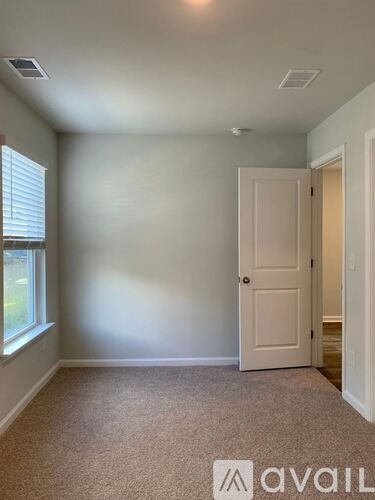 A room with a carpeted floor, a door, and a window with blinds.
