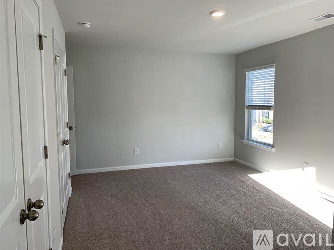 A room with a carpeted floor, a door, and a window with blinds.