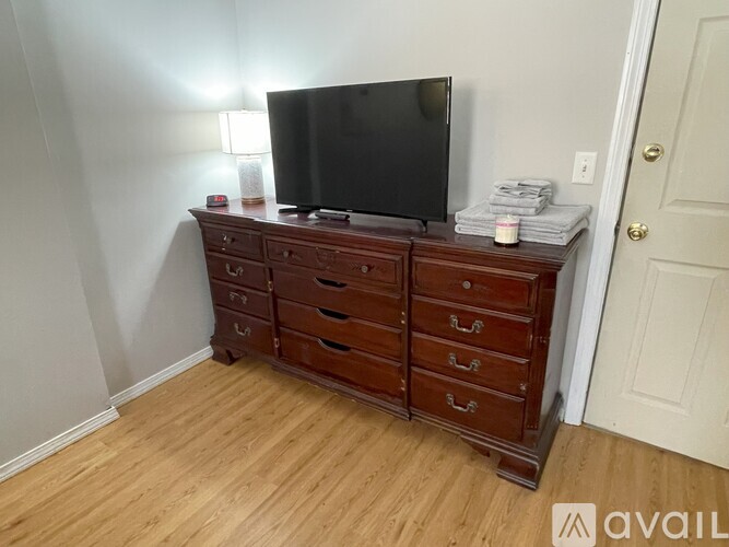 A black television is on a wooden dresser with a white door behind it.