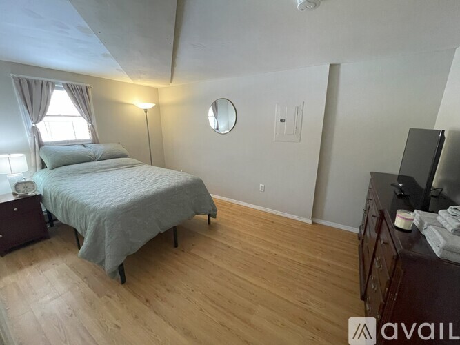 A bedroom with a bed, nightstand, and a wooden floor.