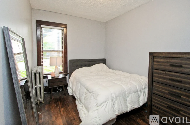 A bedroom with a white bedspread and a wooden dresser.