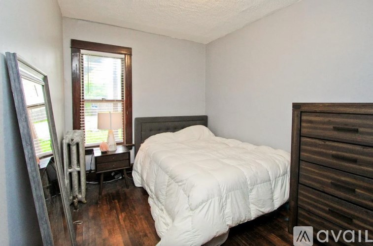 A bedroom with a white bedspread and a wooden dresser.