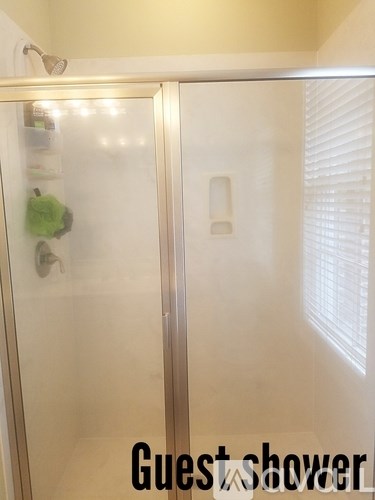 A guest shower with a glass door and a towel hanging on the shower head.