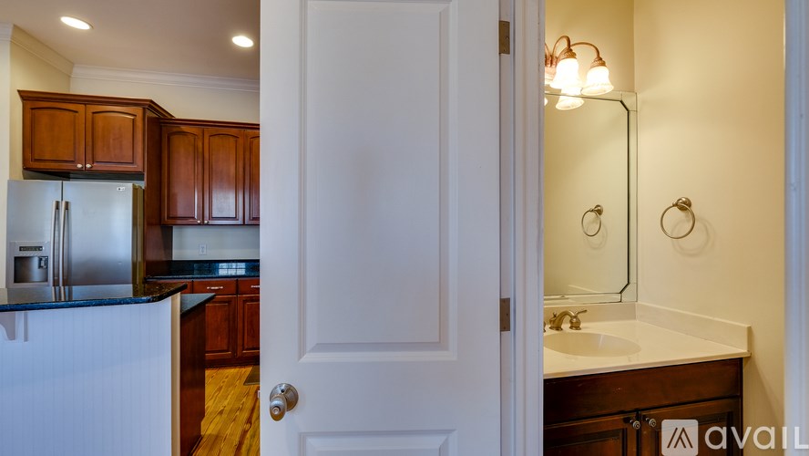 A white door is open to a kitchen with wooden cabinets and a white countertop.