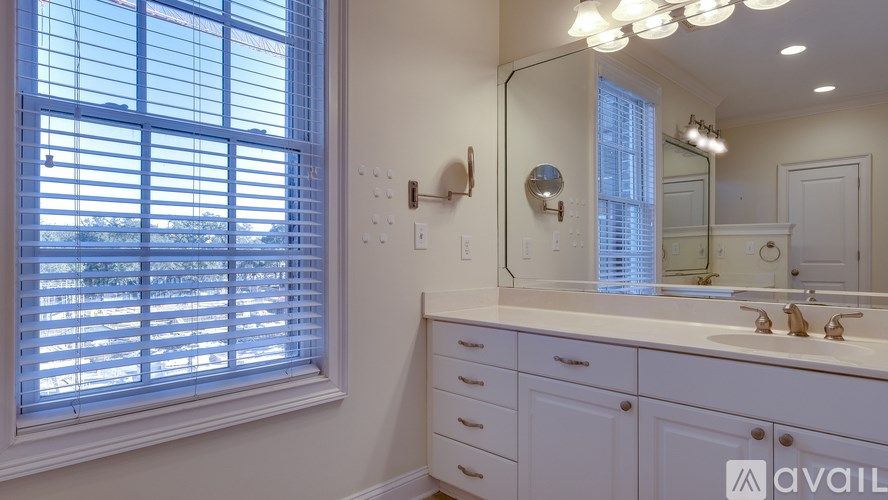 A bathroom with a large mirror, a sink, and a window with blinds.