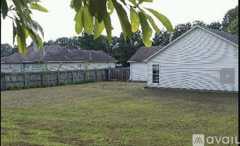 A white house with a grey roof is surrounded by a fence and green grass.