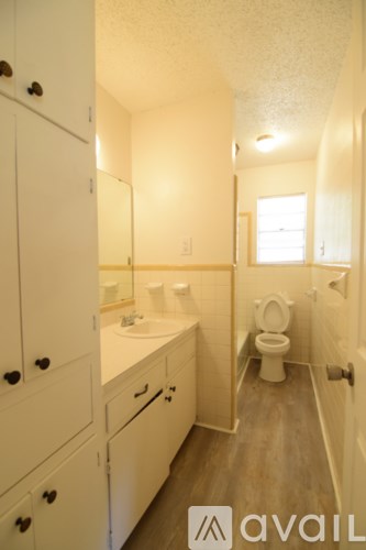 A bathroom with a toilet, sink, and cabinets.