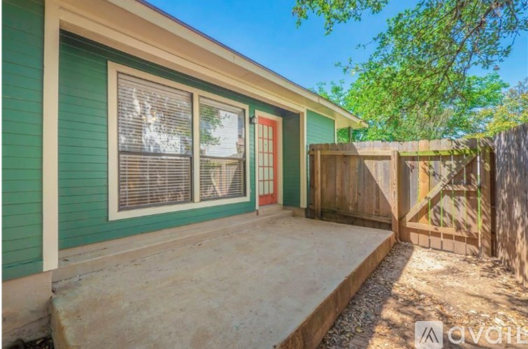 A green house with a red door and a wooden fence.