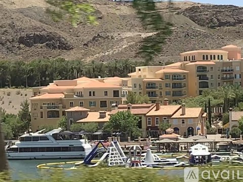 A large building with a red roof is situated next to a body of water with a boat in front of it.