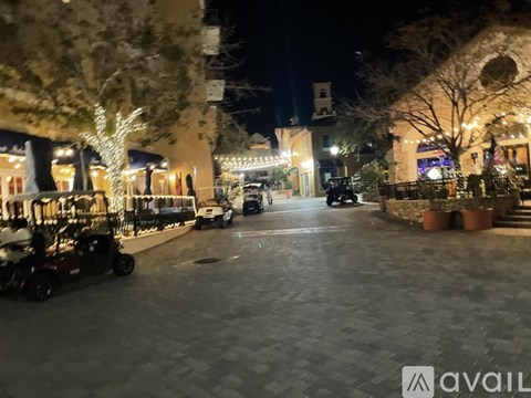 A street view at night with a lit up tree and a car parked on the side.