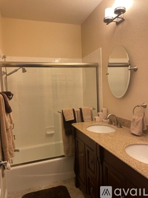 A bathroom with a glass shower door and a round mirror above the sink.