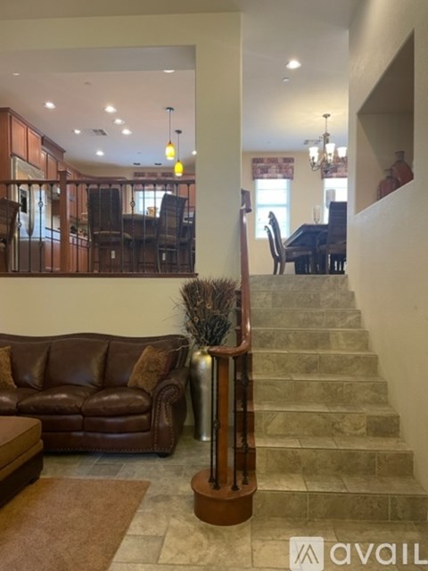 A living room with a brown leather couch and a staircase leading to a dining area.