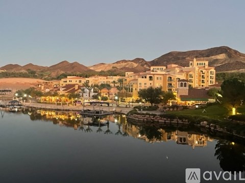 A serene evening view of a waterfront town with buildings and mountains in the background.