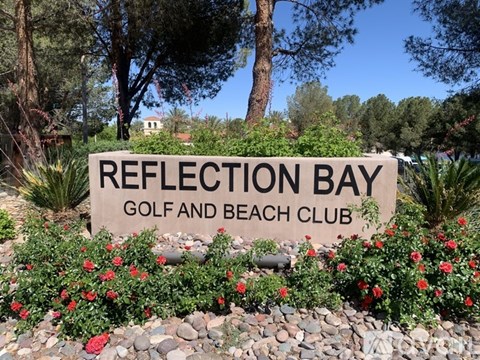 A sign for Reflection Bay Golf and Beach Club is surrounded by red flowers and greenery.