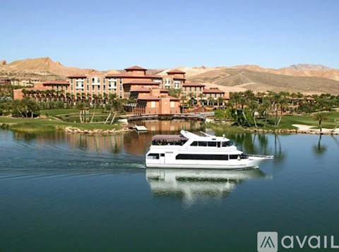 A white yacht is sailing on a lake in front of a large red building.