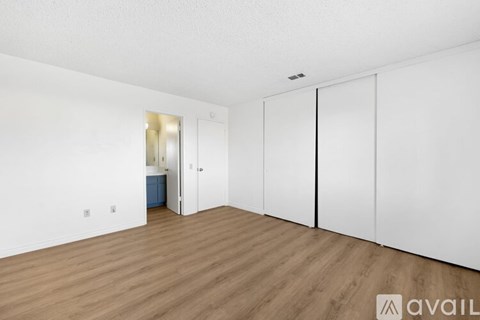 A room with white walls and wooden flooring, featuring a white door and a white wardrobe.