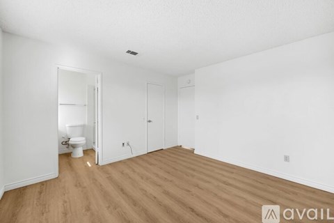 A room with wooden floors and white walls, with a toilet visible in the corner.