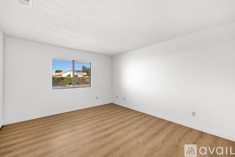 Empty room with wooden floor and a window showing a view of a house.