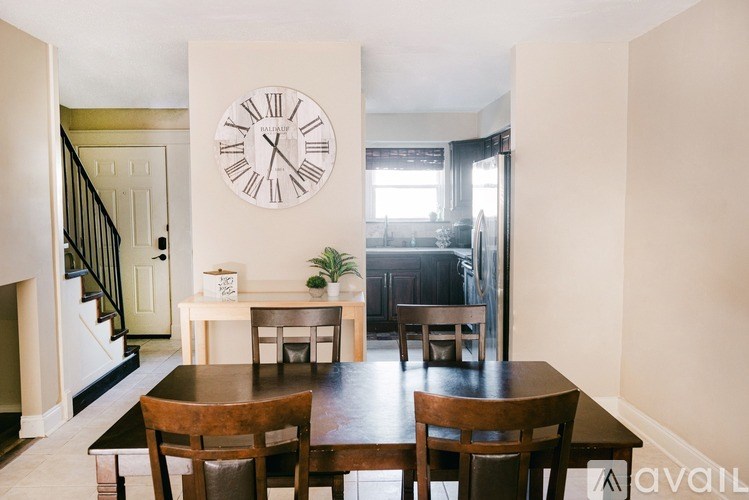 A large wall clock hangs above a dining table in a room.