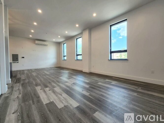 A spacious room with wooden flooring and three windows.