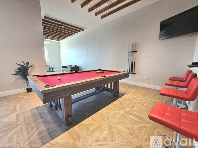 A pool table with red seating is in the middle of a room with wooden flooring and a ceiling with wooden beams.