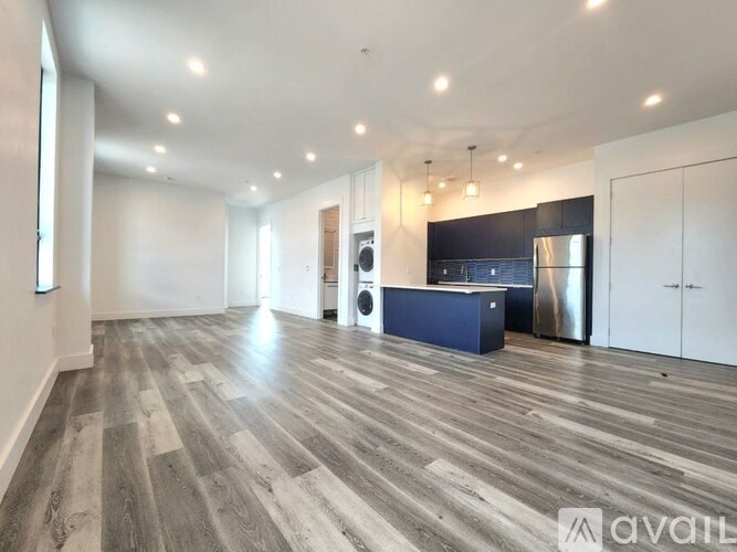 A spacious room with wooden flooring and a kitchen area in the background.