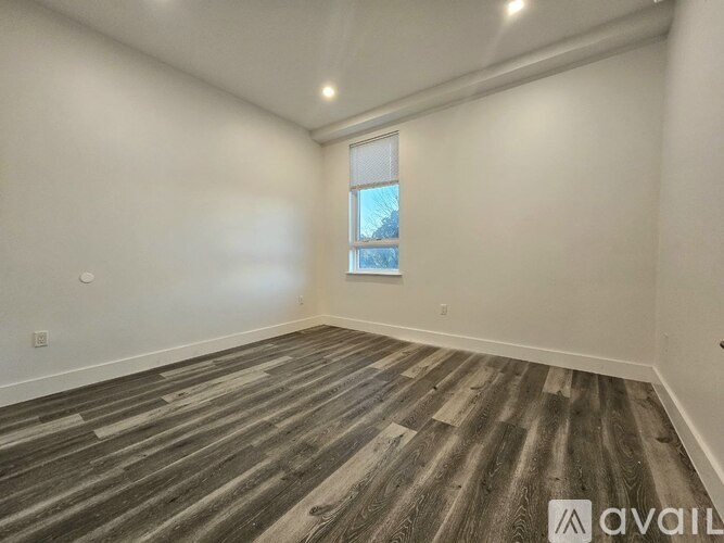 A room with wooden flooring and a window showing a view of trees outside.