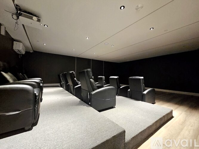 A row of black cinema seats are arranged in a dark room.