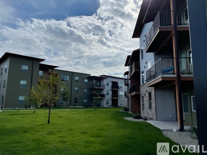 A grassy area in front of apartment buildings with a tree and a cloudy sky.