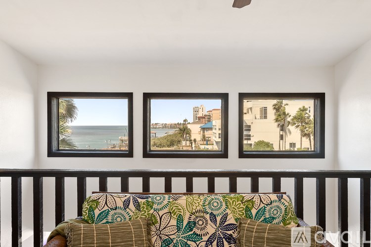 A couch with a green and blue patterned cushion sits in front of three framed pictures on a balcony.