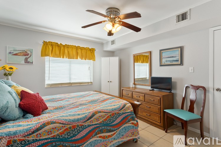 A bedroom with a bed, dresser, chair, and a ceiling fan.