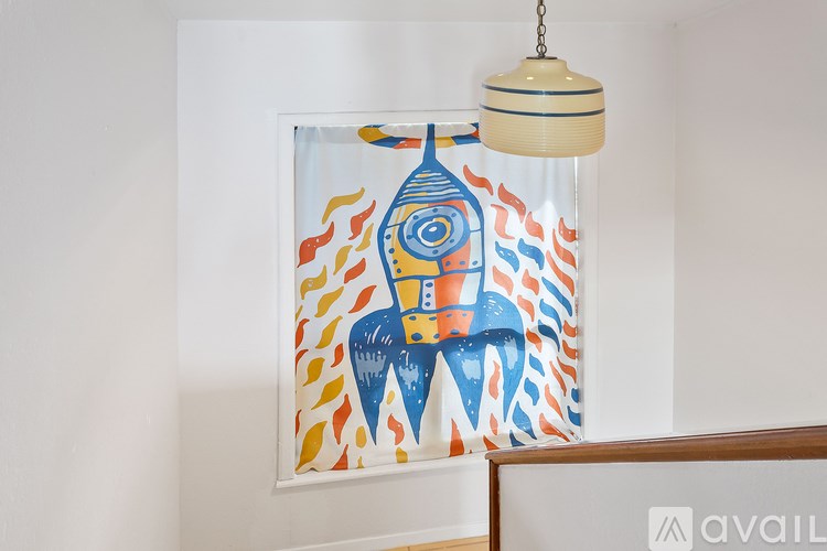 A painting of a blue and orange rocket ship hangs on a white wall.
