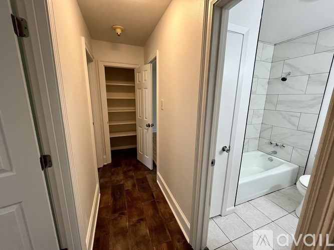 A hallway with a white door and a white bathroom with a white tub.