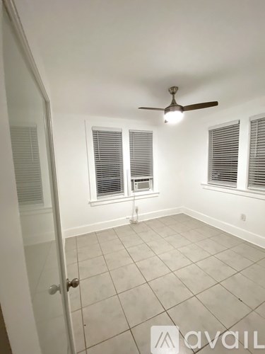 A room with a ceiling fan and three windows with blinds.