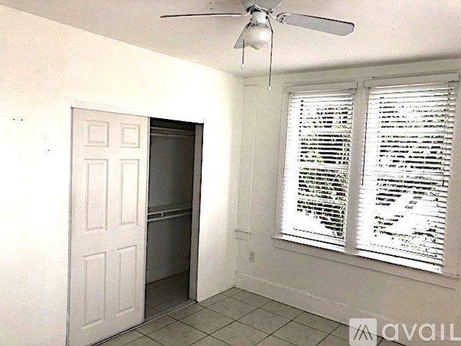 A room with a ceiling fan and a door leading to a darker room.
