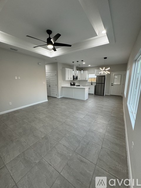 A spacious room with a ceiling fan and a kitchen area in the background.
