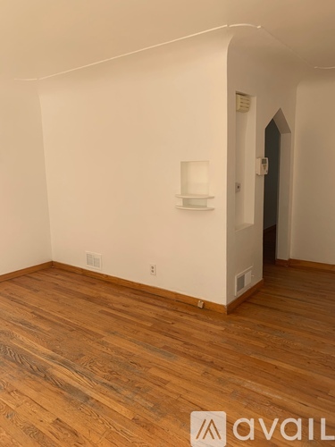A room with wooden flooring and a white wall with a shelf and a door.
