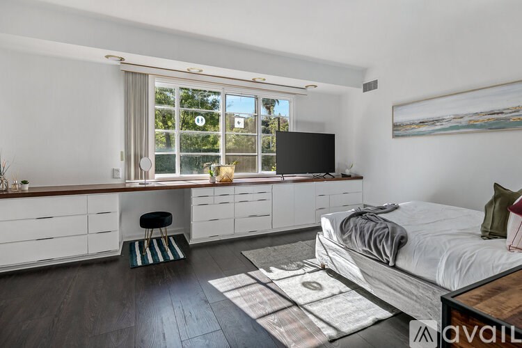 A bedroom with a bed, a TV, and a window with a view of trees.